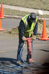 A worker using a heavy-duty drill on concrete ground