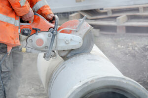  A worker at a construction site cutting a concrete drainage pipe with a concrete saw